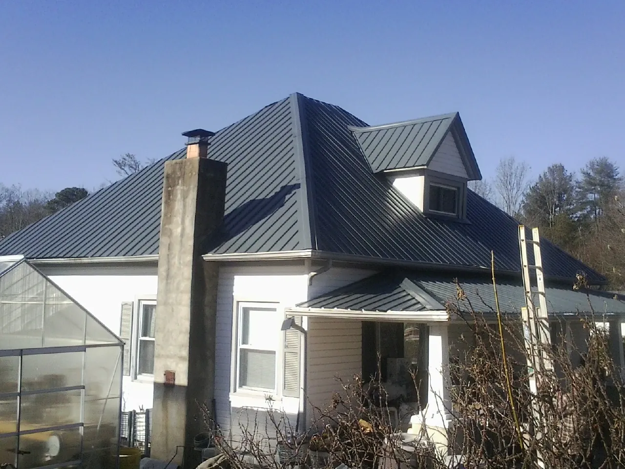 Dark blue standing seam metal roof on a white farmhouse with dormer — Slate & Tile Roof Repair by Roofing Brothers in Ontario