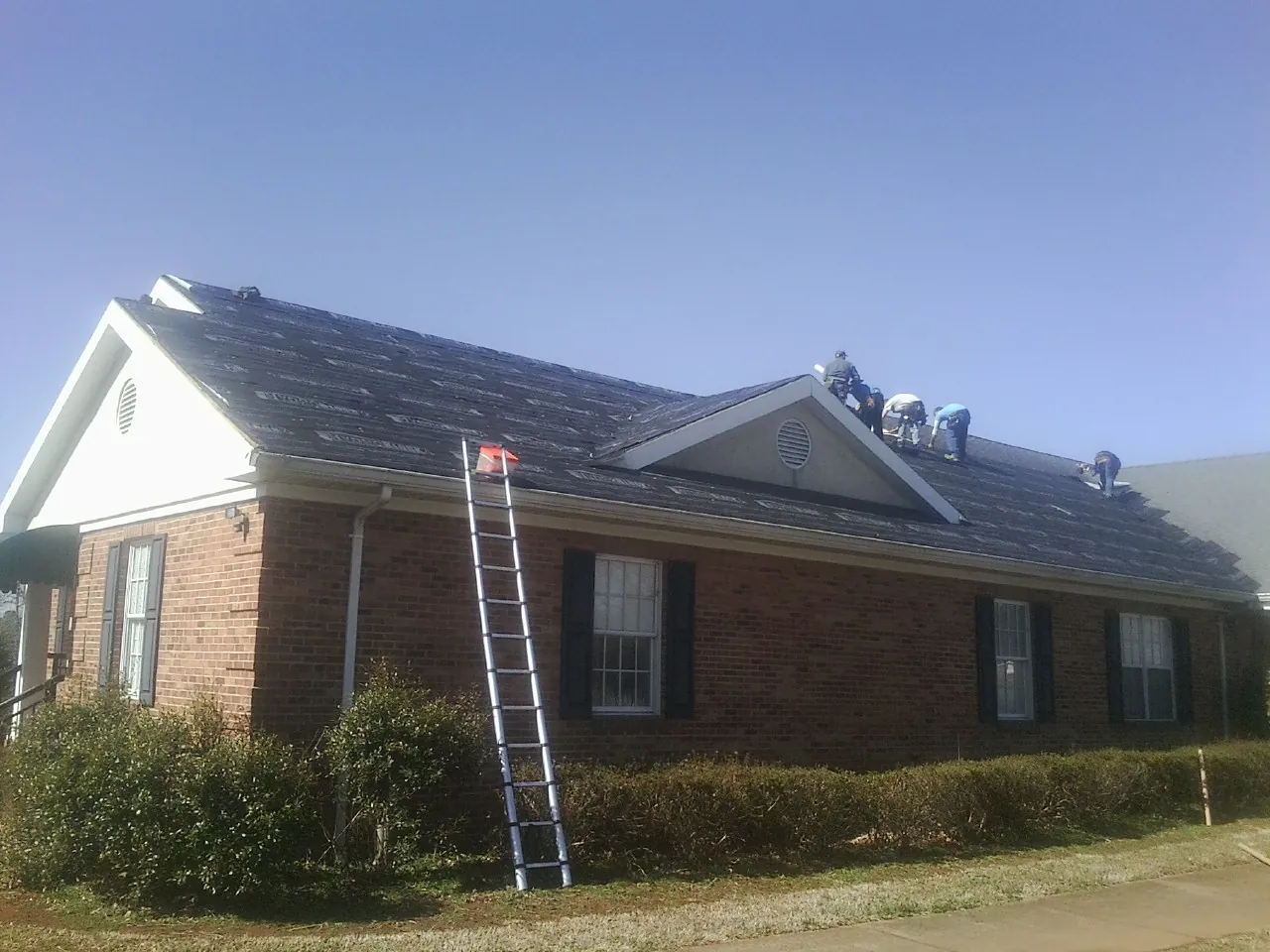 Crew tearing shingles off a brick ranch roof with a ladder set — Emergency Roof Repair work by our crew in Ontario