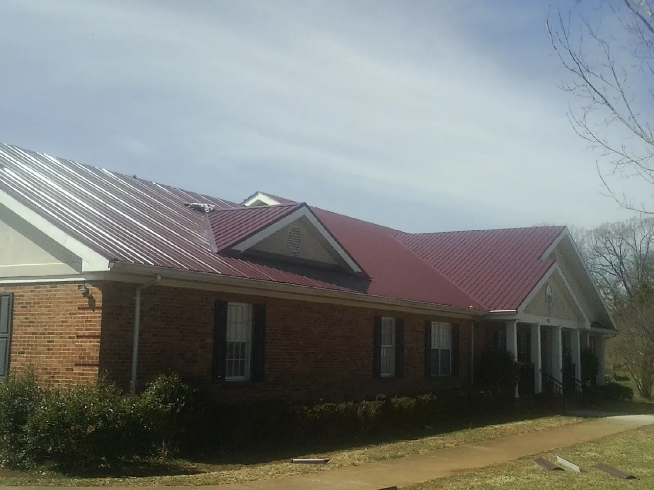 Red metal roof with gabled entries on a long brick building, from a Hail Damage Roof Repair job in Ontario